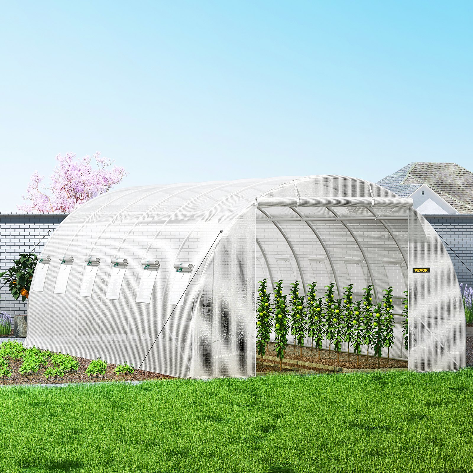 VEVOR tunnel greenhouse with plants inside, located in a backyard with a brick wall and lush greenery.