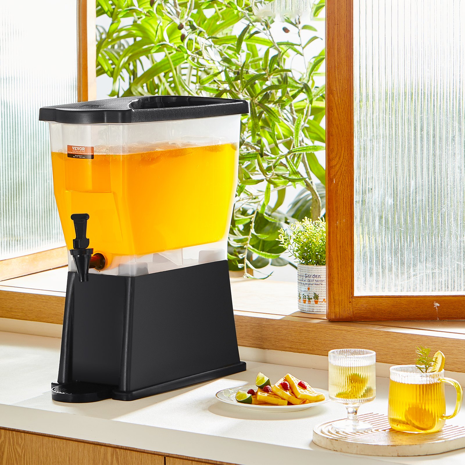 VEVOR beverage dispenser on countertop with orange drink, next to glasses and snacks, plants in the background.