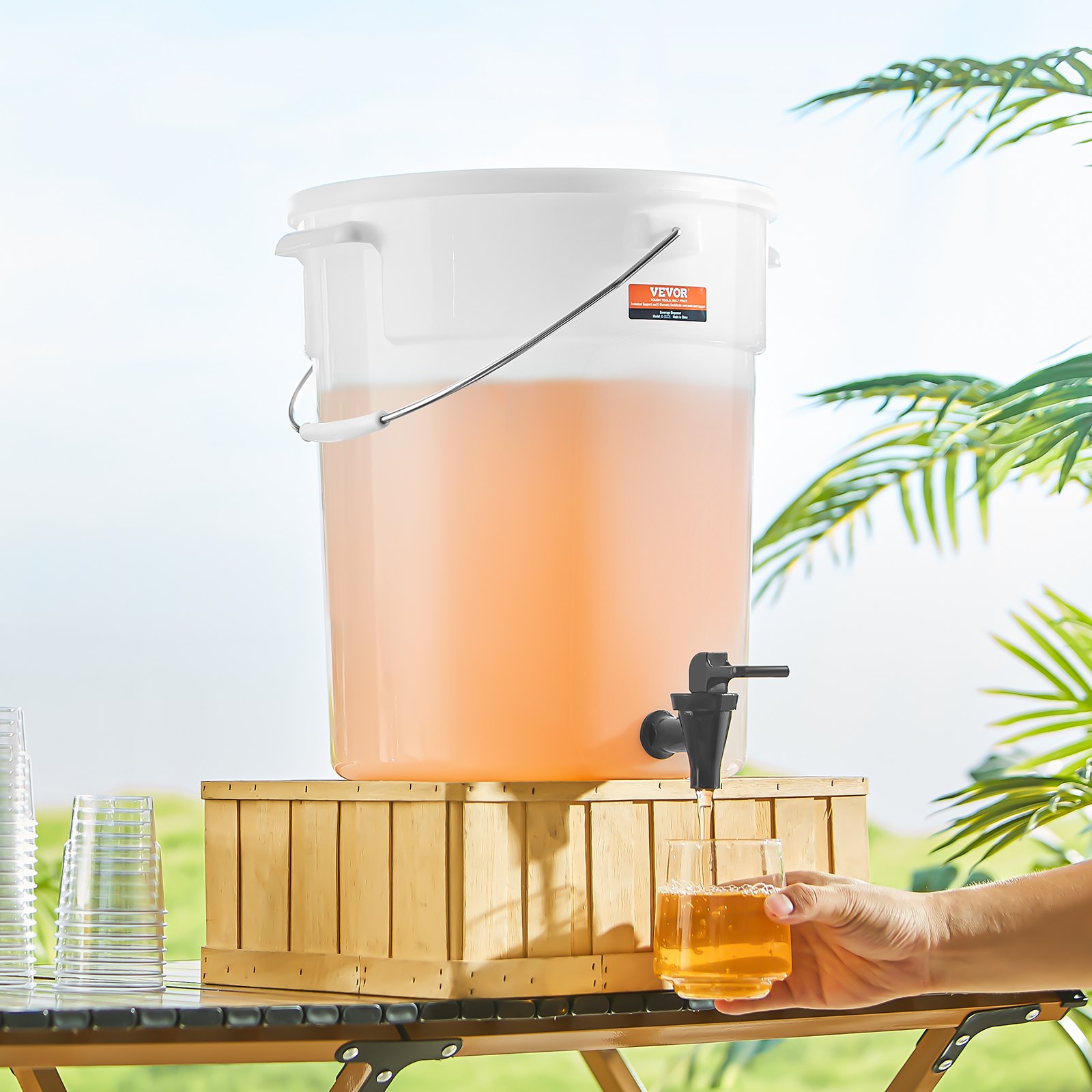 VEVOR beverage dispenser with lemonade, on a wooden stand outdoors, with glasses and hand pouring drink.