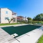 VEVOR pool safety cover on a sunny day over an outdoor pool with a villa and manicured garden.