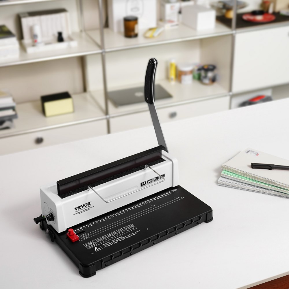 VEVOR binding machine on a white desk, lever upright, with spiral notebooks and pen in a modern office.