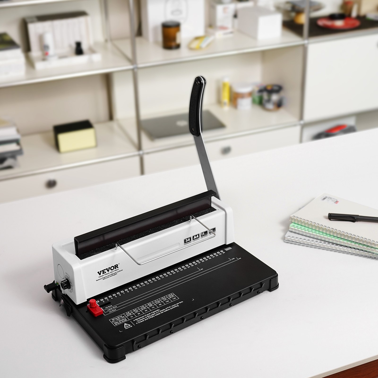 VEVOR binding machine on a white desk, lever upright, with spiral notebooks and pen in a modern office.