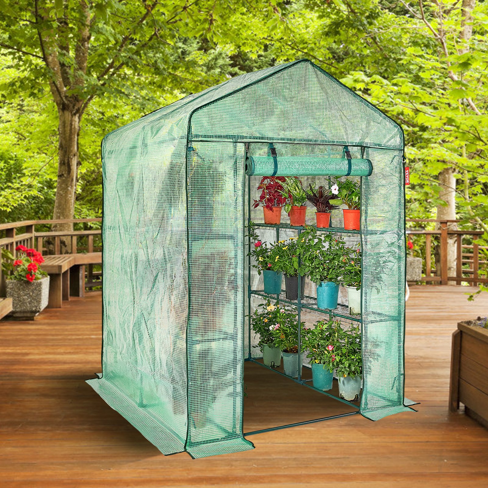 VEVOR walk-in greenhouse, plants in pots inside, on a wooden deck surrounded by lush greenery.
