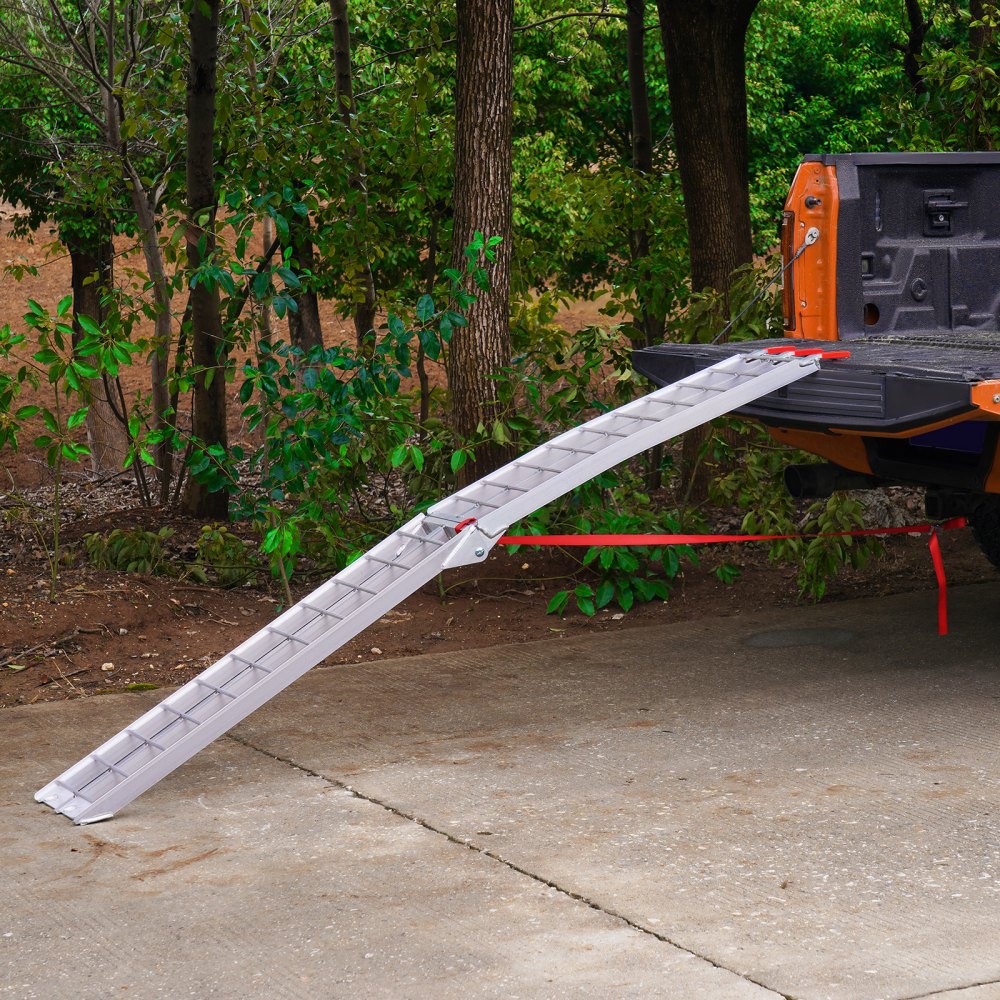 aluminum VEVOR motorcycle loading ramp attached to an orange truck bed in front of a forest background.