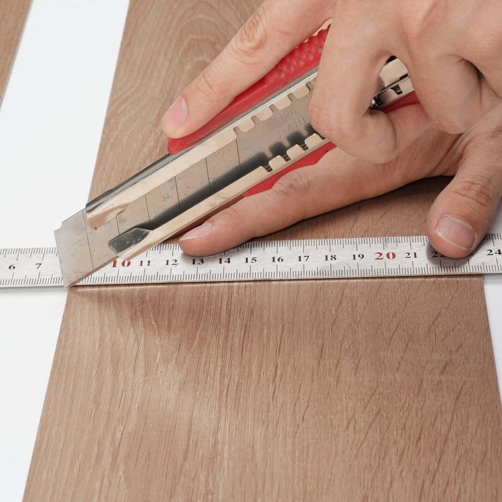 cutting VEVOR self adhesive vinyl floor tiles with a utility knife and measuring tape.