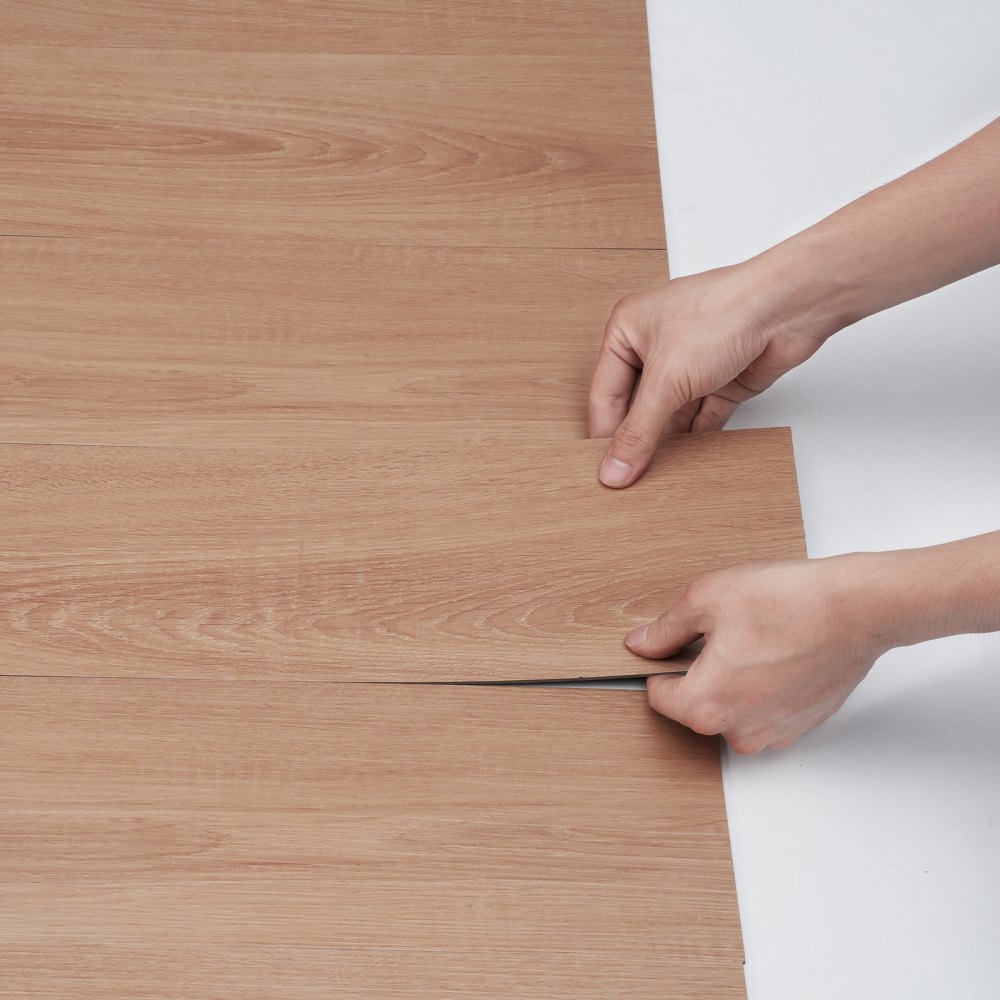 hands installing VEVOR self adhesive vinyl floor tiles with a wood grain texture.